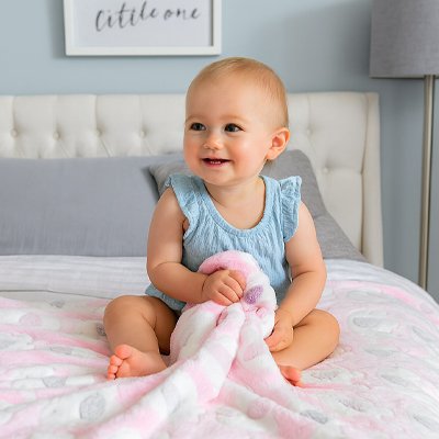 Bébé assis sur un tapis moelleux, tenant une couverture rose à motifs d’oursons – confort et douceur absolus.