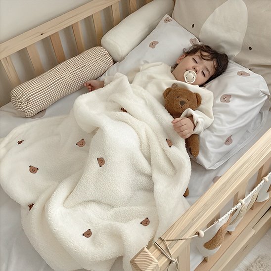 Bébé endormi sous une couverture blanche moelleuse à petits motifs marron – confort et sécurité pendant le sommeil.