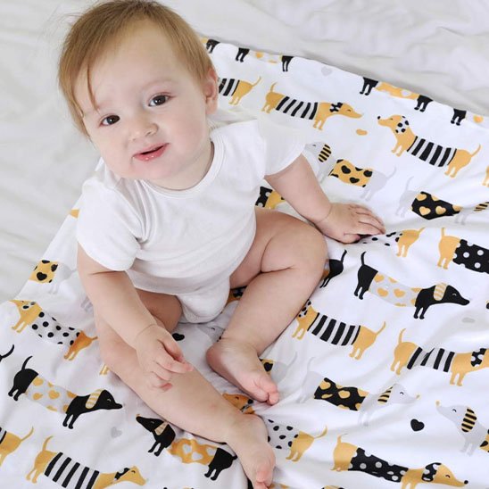 Bébé assis sur une couverture blanche à motifs d’animaux jaunes et noirs – couverture confortable pour chambre de bébé.