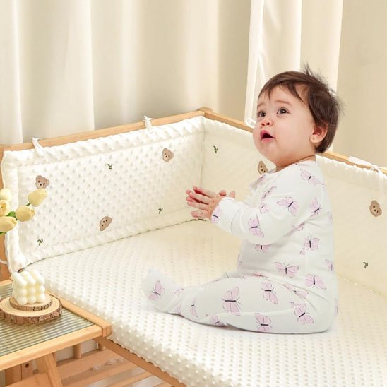 Bébé allongé dans un lit à barreaux avec tour de lit rembourré beige à motif d’ourson – sécurité et confort assurés