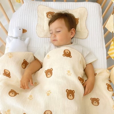Bébé endormi sous une couverture blanche à motifs d’oursons marron – chaleur et douceur pour la nuit.