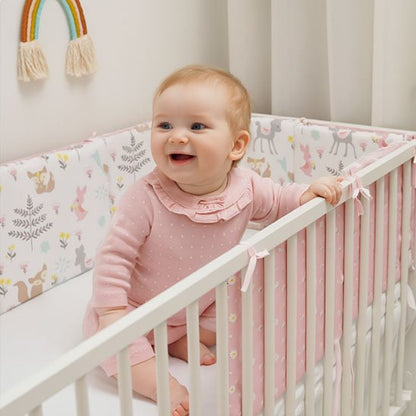 Bébé riant dans un lit à barreaux avec tour de lit rose rembourré – ambiance douce et apaisante
