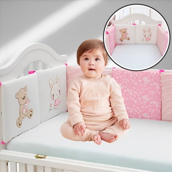 Bébé souriant assis dans un lit avec tour de lit rembourré rose et motif d’ourson brodé – confort et tendresse.