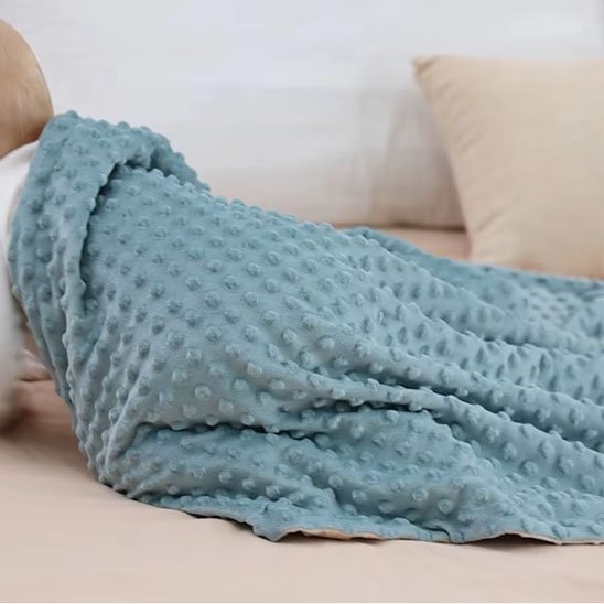 Enfant détendu sous une grande couverture bleue texturée, parfaite pour les moments cocooning à la maison