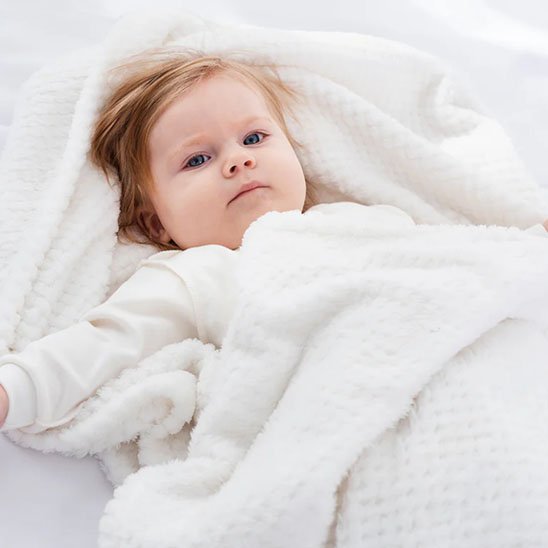 Bébé blond emmitouflé dans une couverture couleur crème ultra-douce, parfaite pour garder la chaleur