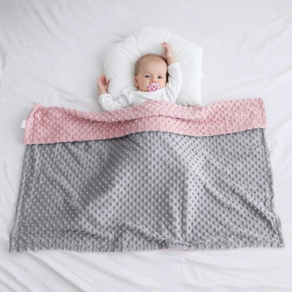 Bébé allongé paisiblement sous une couverture double face rose et grise, parfaite pour le sommeil et l’emmaillotage