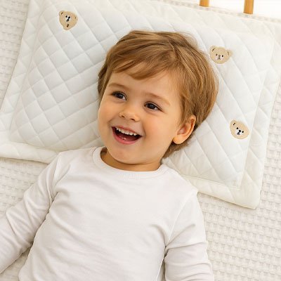 Enfant riant, allongé sur un oreiller bébé doux en coton – confort idéal pour les siestes et les nuits paisibles.