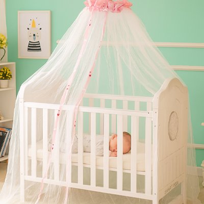 Bébé endormi paisiblement dans un lit à baldaquin équipé d’une moustiquaire blanche à bord rose, protégeant contre les moustiques et insectes.