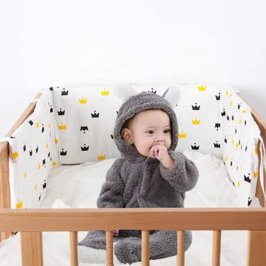 Tour de lit bébé à motifs jaunes, noirs avec un bébé souriant, le doigt dans la bouches pour une touche douce et sécurisante dans la chambre.