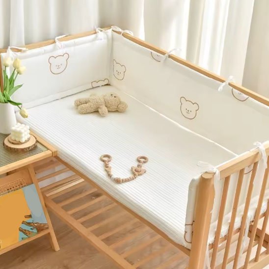 Lit de bébé en bois équipé d’un tour de lit beige à motif d’ourson, décor naturel et apaisant pour la chambre de bébé.