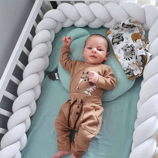 Tresse de lit bébé vert et beige protégeant le bébé allongé dans son lit avec douceur et sécurité.